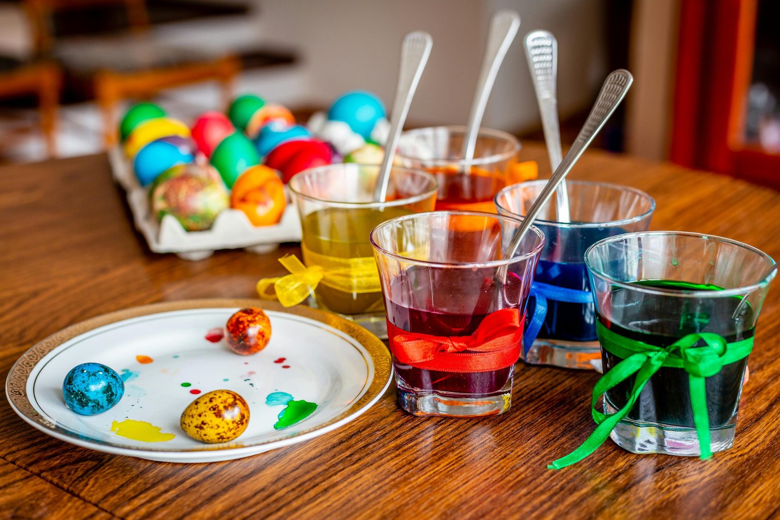 Colorful Easter egg dyeing setup with glasses, ribbons, and painted eggs on a wooden table.